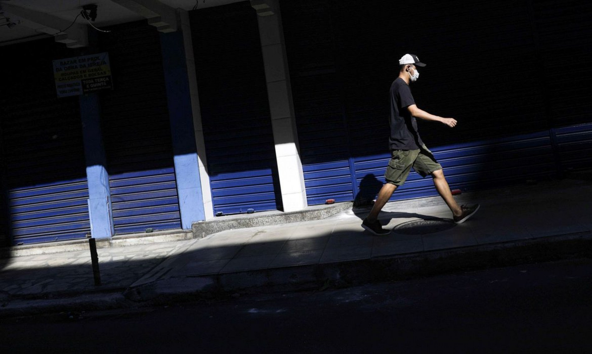 Um homem usando uma máscara protetora passa por um comércio fechado na cidade de Niterói 