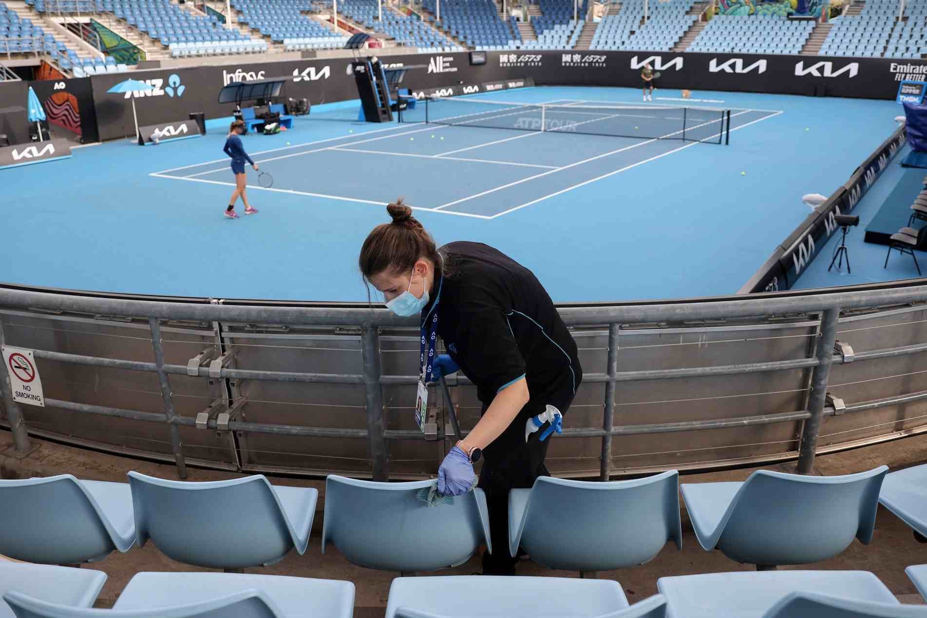 Na imagem, mulher limpa as áreas dos assentos, em aquecimento no Melbourne Park, em um dos preparativos para o Aberto da Austrália  (Fevereiro/2021)
