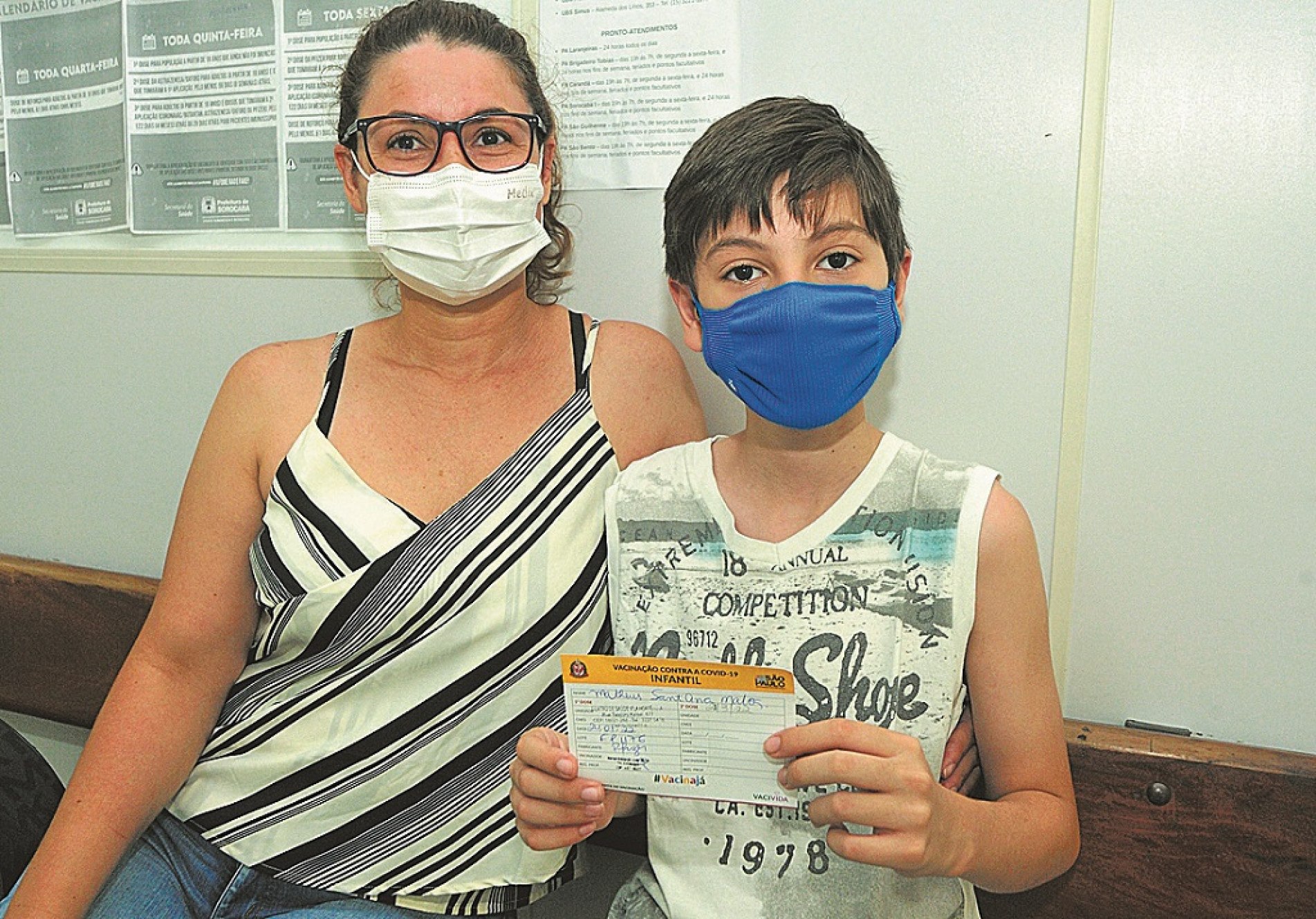 Ao lado da mãe Fabiane, Mateus Santana Matos, de 11 anos, mostra o comprovante da vacina 