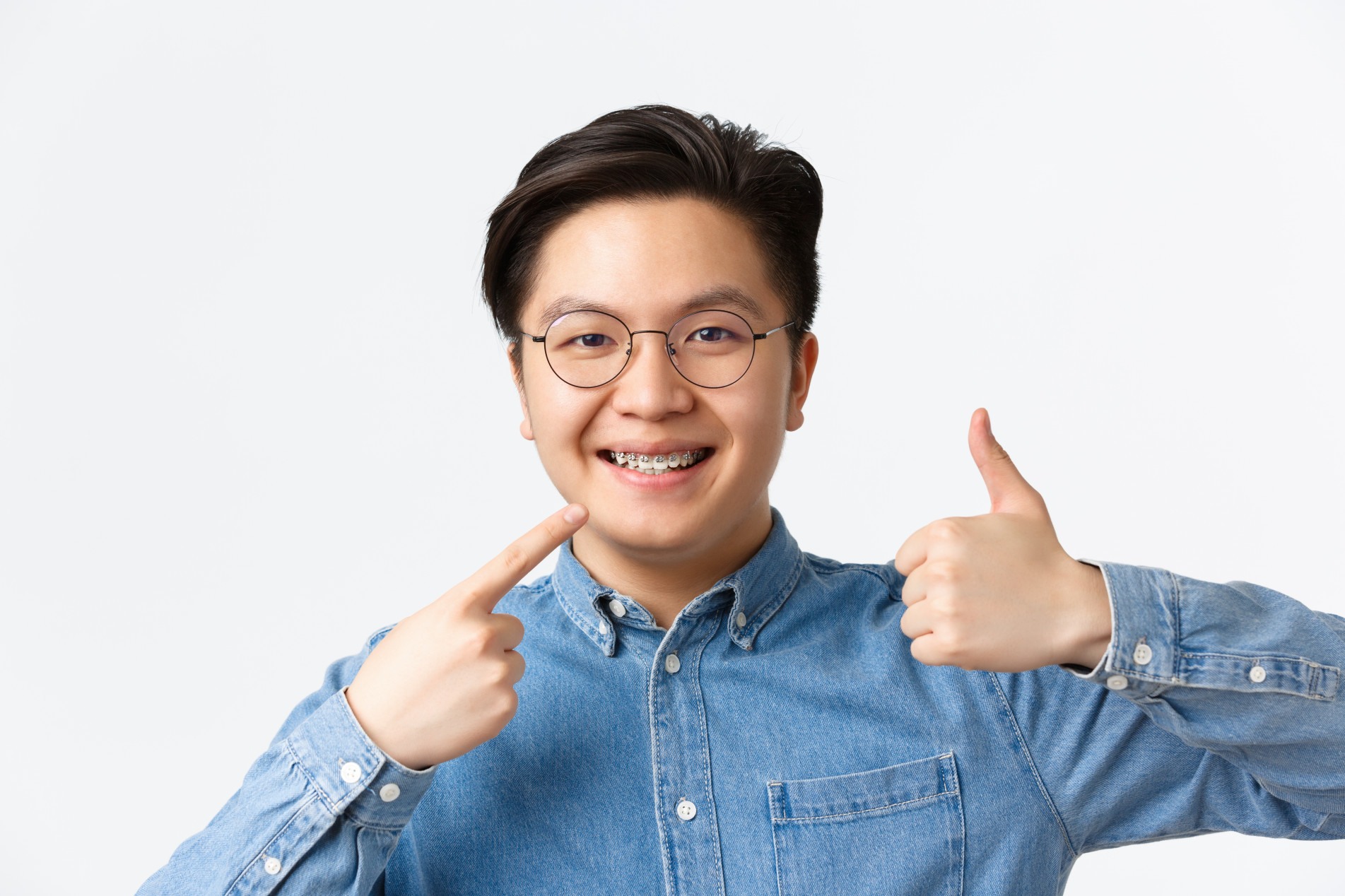  Orthodontics and stomatology concept. Close-up of satisfied asian guy, dental clinic client smiling happy and pointing at his dental braces and showing thumbs-up in approval, recommend.
    