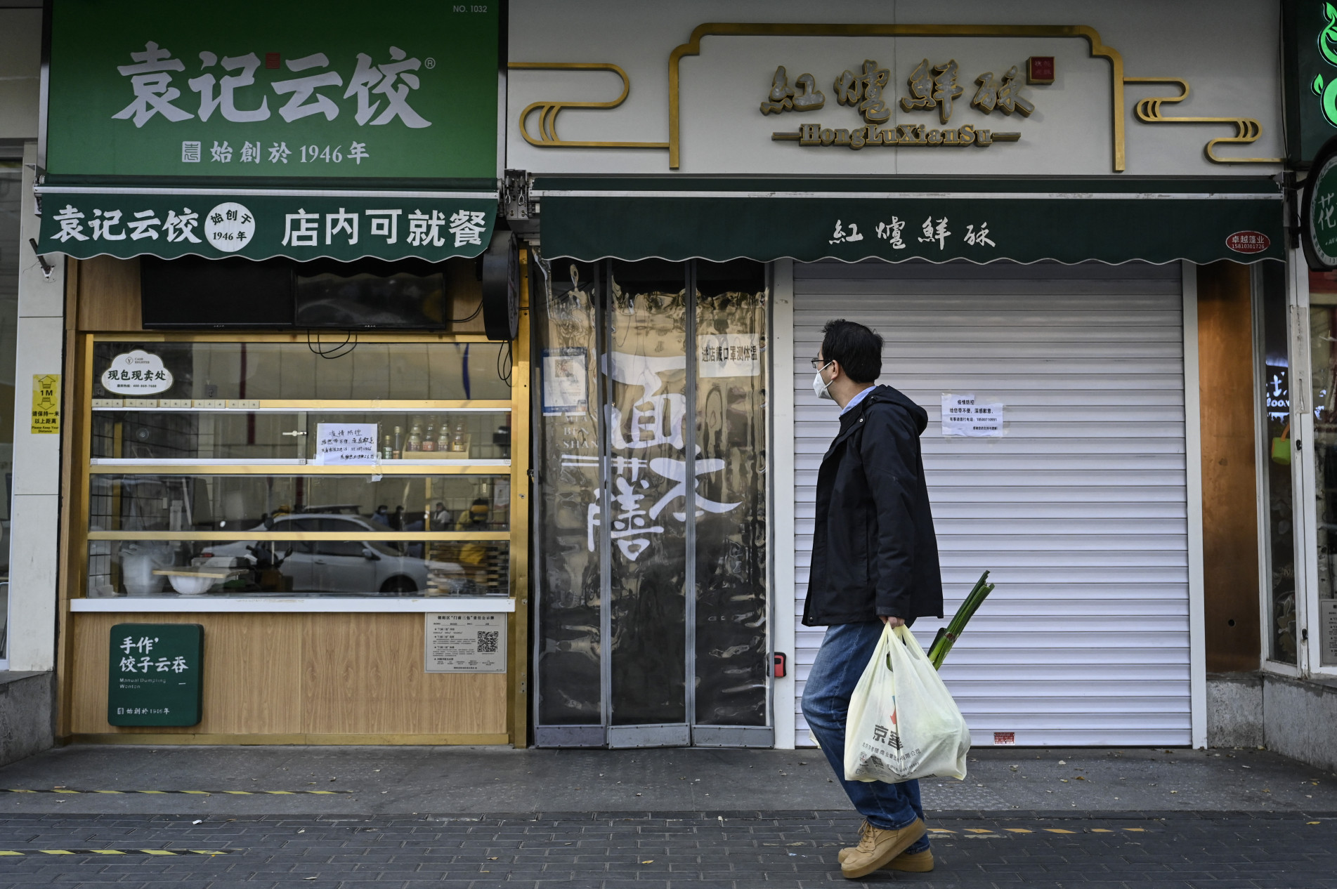  A man carrying a bag of vegetables walks past closed shops in Beijing?s Chaoyang district due to Covid-19 coronavirus restrictions on November 19, 2022. (Photo by Jade GAO / AFP)