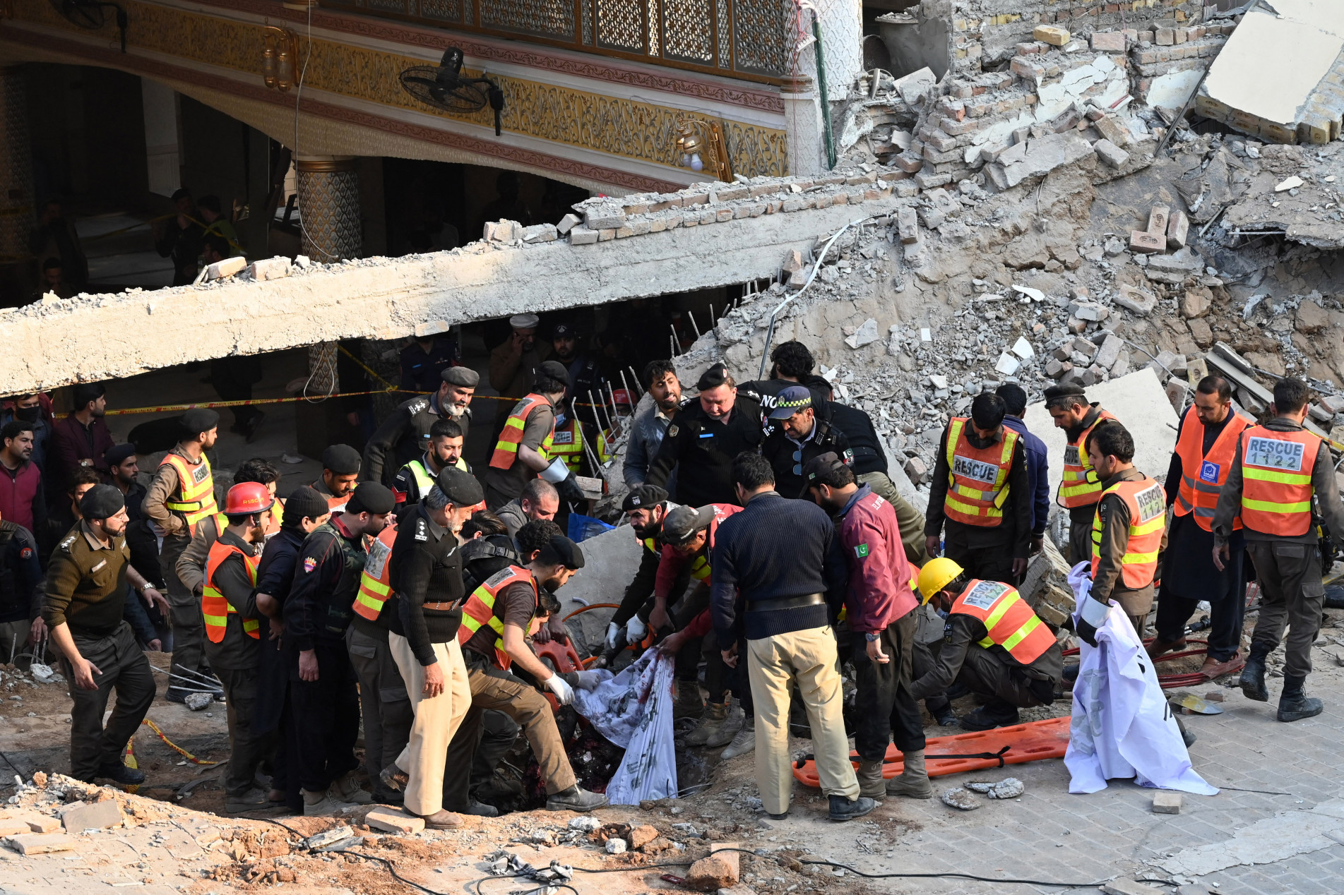  Rescue workers carry the remains of the blast victims from the debris of a damaged mosque after a blast inside the police headquarters in Peshawar on January 30, 2023. - A blast at a mosque inside a police headquarters in Pakistan on January 30 killed at least 25 worshippers and wounded 120 more, officials said. (Photo by Abdul MAJEED / AFP)