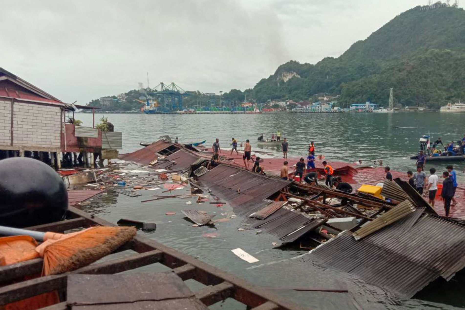  People stand on the roofing of collapsed shops in the port after a 5.1-magnitude earthquake in Jayapura, Indonesia's eastern province of Papua on February 9, 2023. (Photo by FAISAL NARWAWAN / AFP)
      Caption