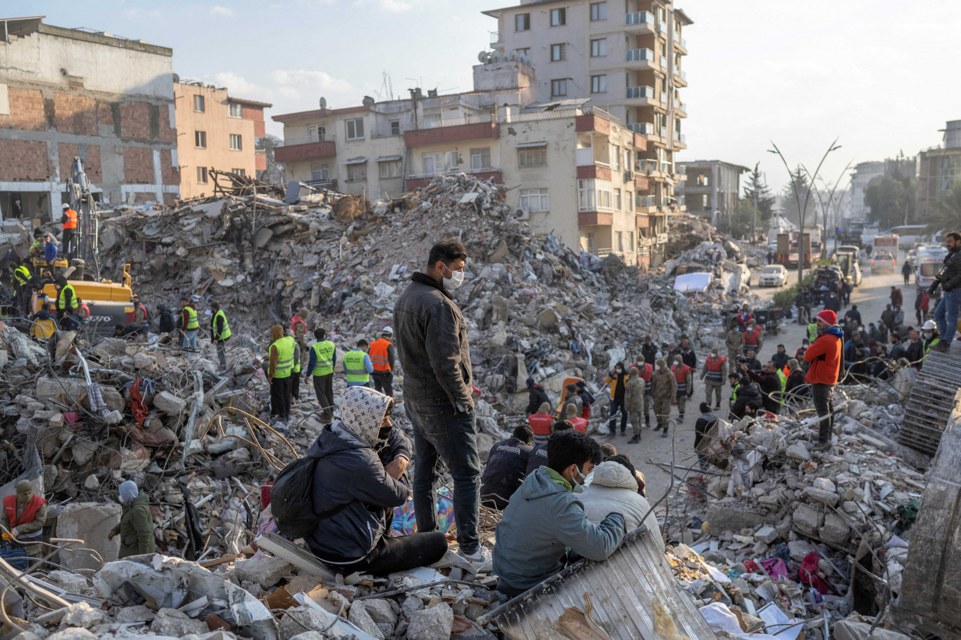  People stand on top of rubble of collapsed buildings during rescue operations  in Hatay on February 12, 2023, after a 7,8 magnitude earthquake struck the border region of Turkey and Syria earlier in the week. (Photo by BULENT KILIC / AFP)
      Caption