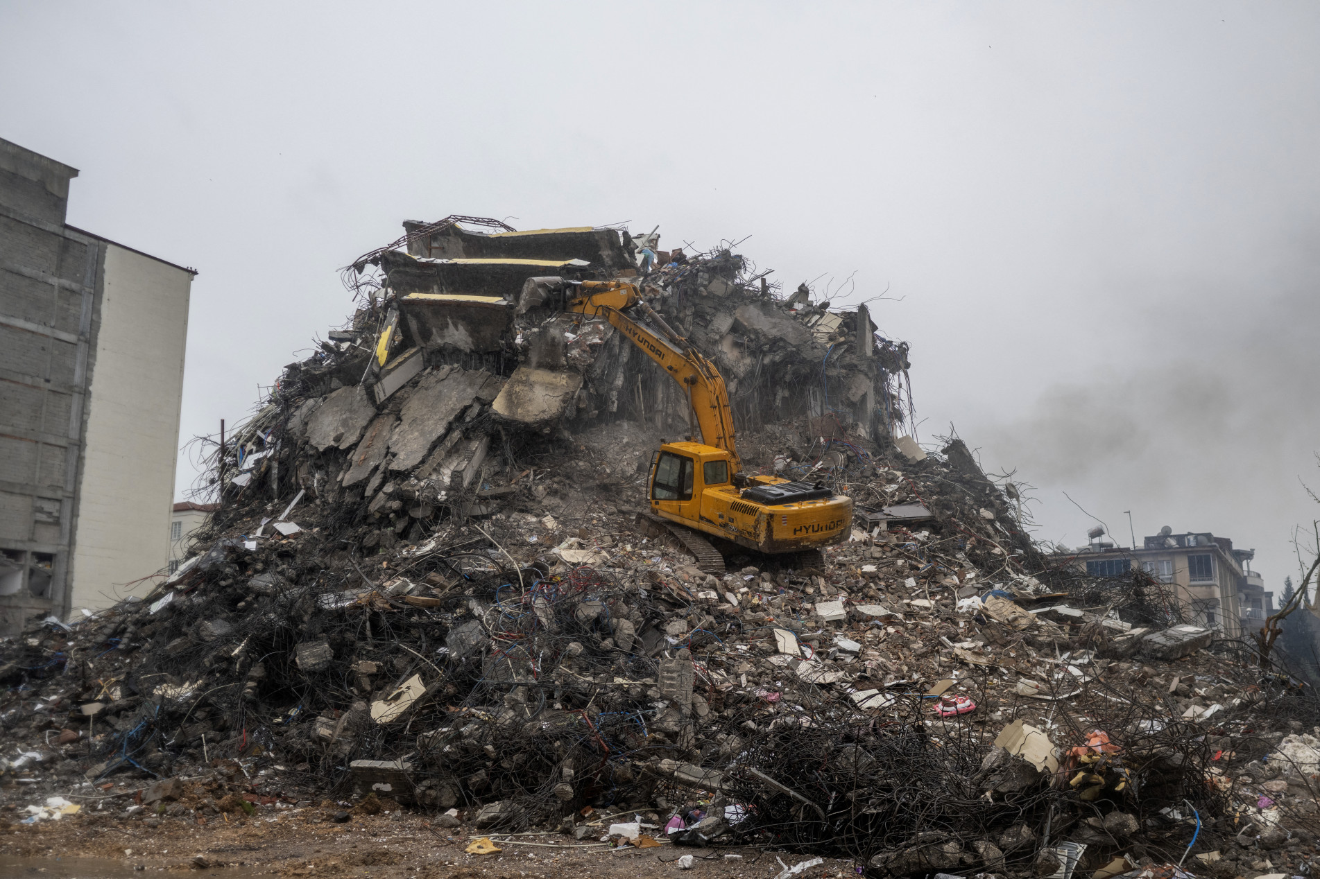  A digger stationed on a mound of rubble breaks down a destroyed building following a massive earthquake last month, in Adiyaman, southeastern Turkey on March 25, 2023. - On February 6, 2023, a 7.8-magnitude earthquake killed more than 50,000 in southeastern Turkey and nearly 6,000 over the border in Syria, leaving entire cities in ruins. Hundreds of thousands of Turkish quake survivors have been moved into tents and container homes across the disaster region, which covers 11 provinces across Turkey's southeast. (Photo by BULENT KILIC / AFP)
      Caption