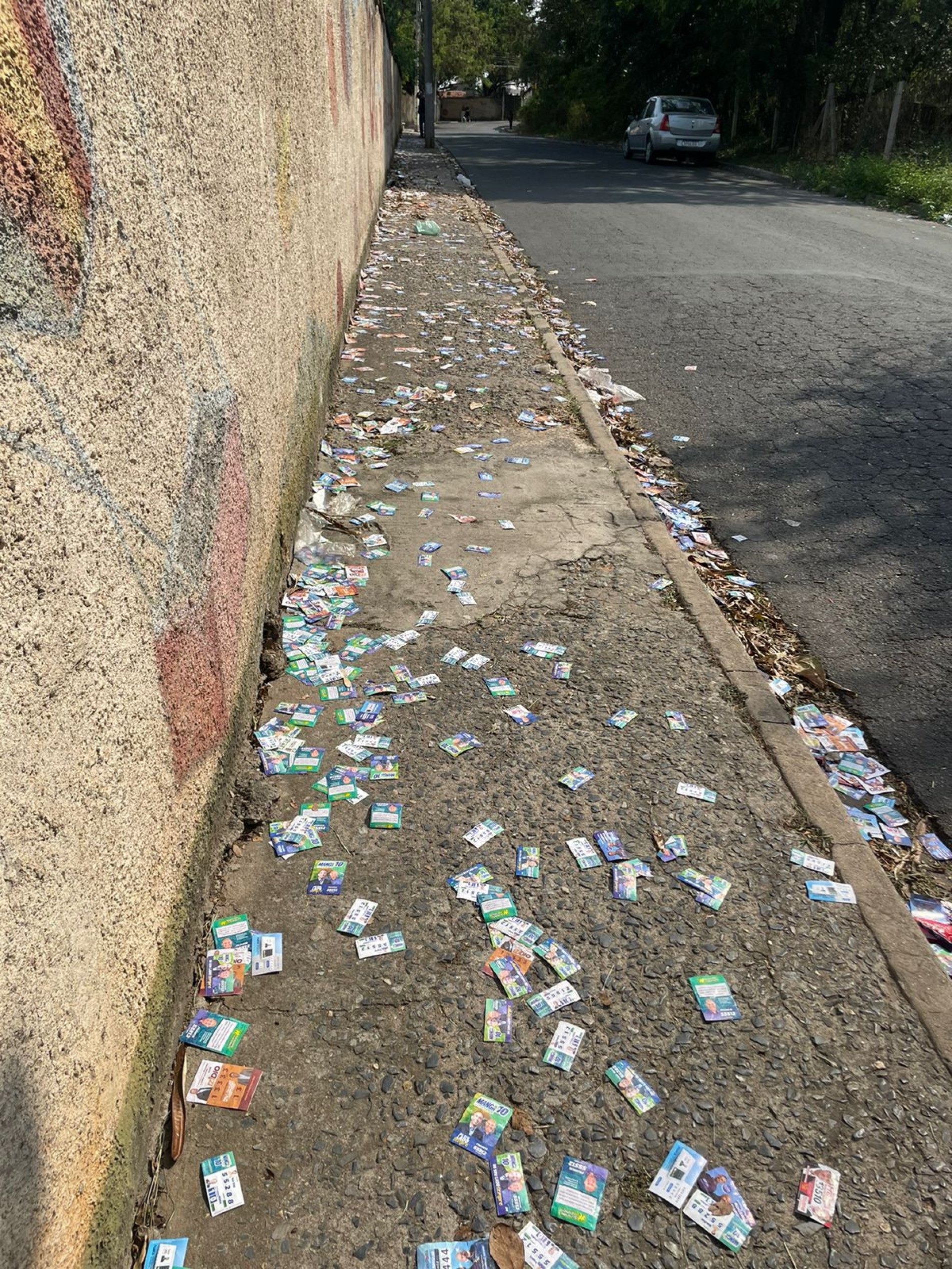Alguns santinhos estão espalhados no chão e na calçada próxima à escola E. E Accácio de Vasconcellos Camargo, no bairro Aparecidinha