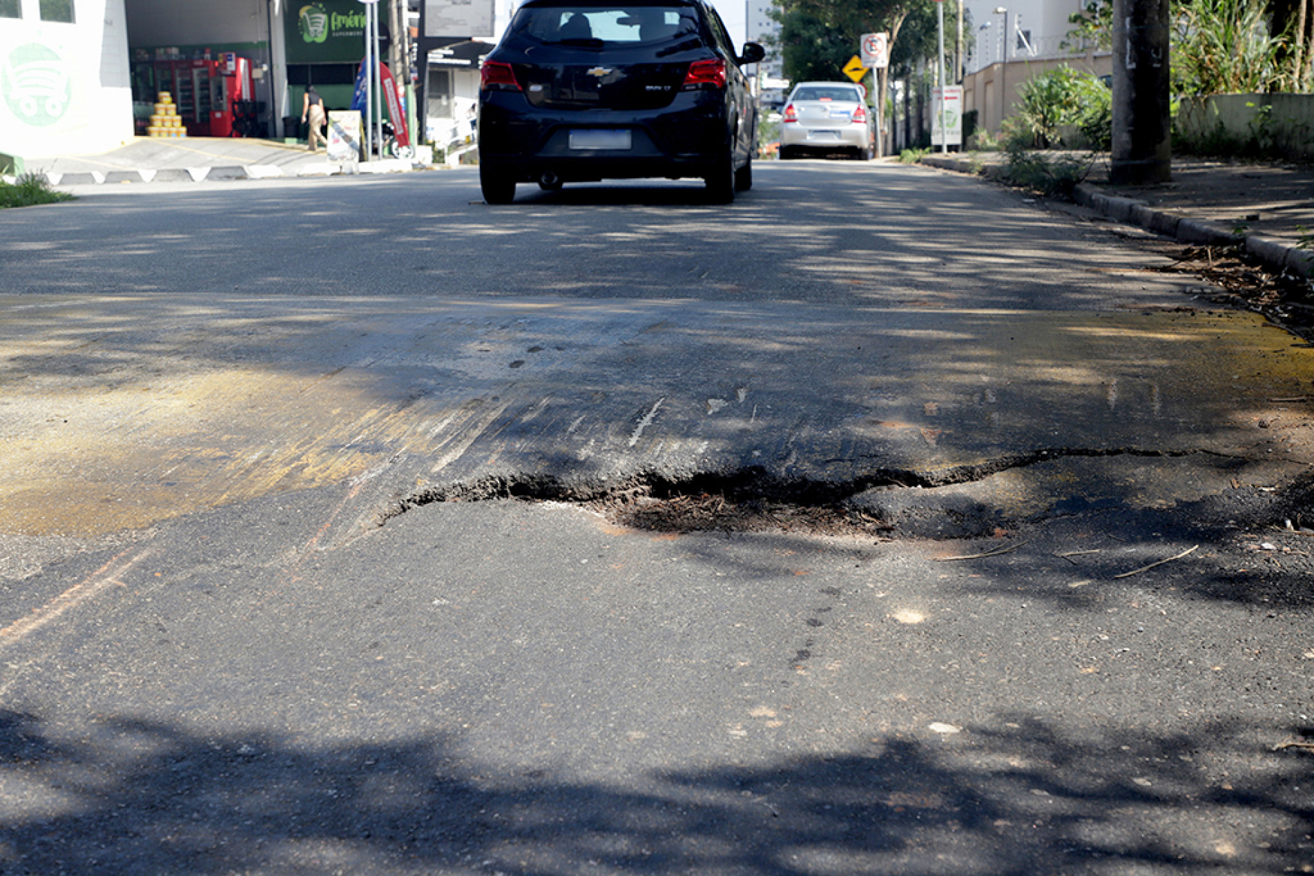 Há rachaduras na via e uma parte do asfalto está cedendo; margem da calçada também está danificada

