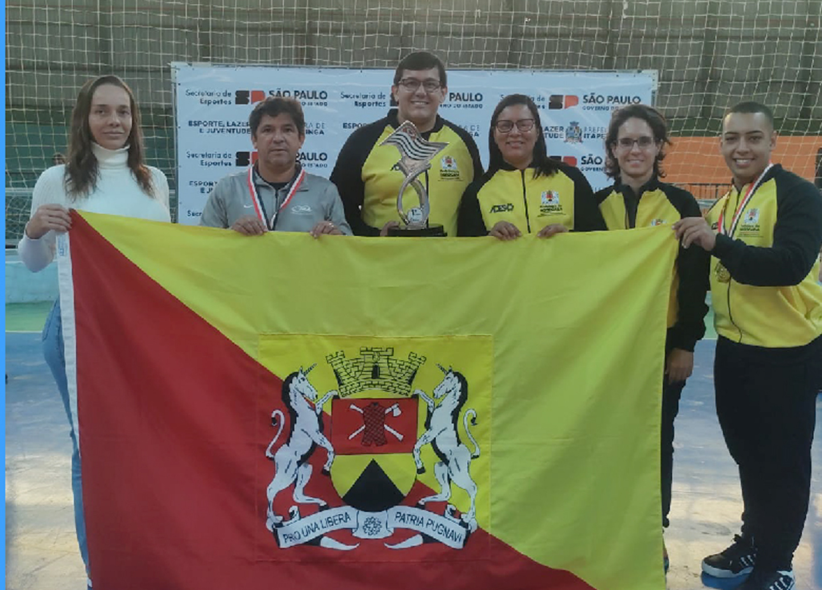 Equipe da Secretaria de Esportes recebe o troféu de campeão e posa com a bandeira do município
