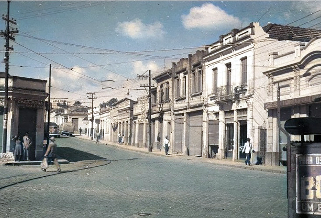 Foto colorizada digitalmente mostra o início da Av. Nogueira Padilha esquina com a av. São Paulo. Nota-se calçamento em paralelepípedos e trilhos de bonde. 
Data e autor: desconhecidos, talvez nos anos 50
