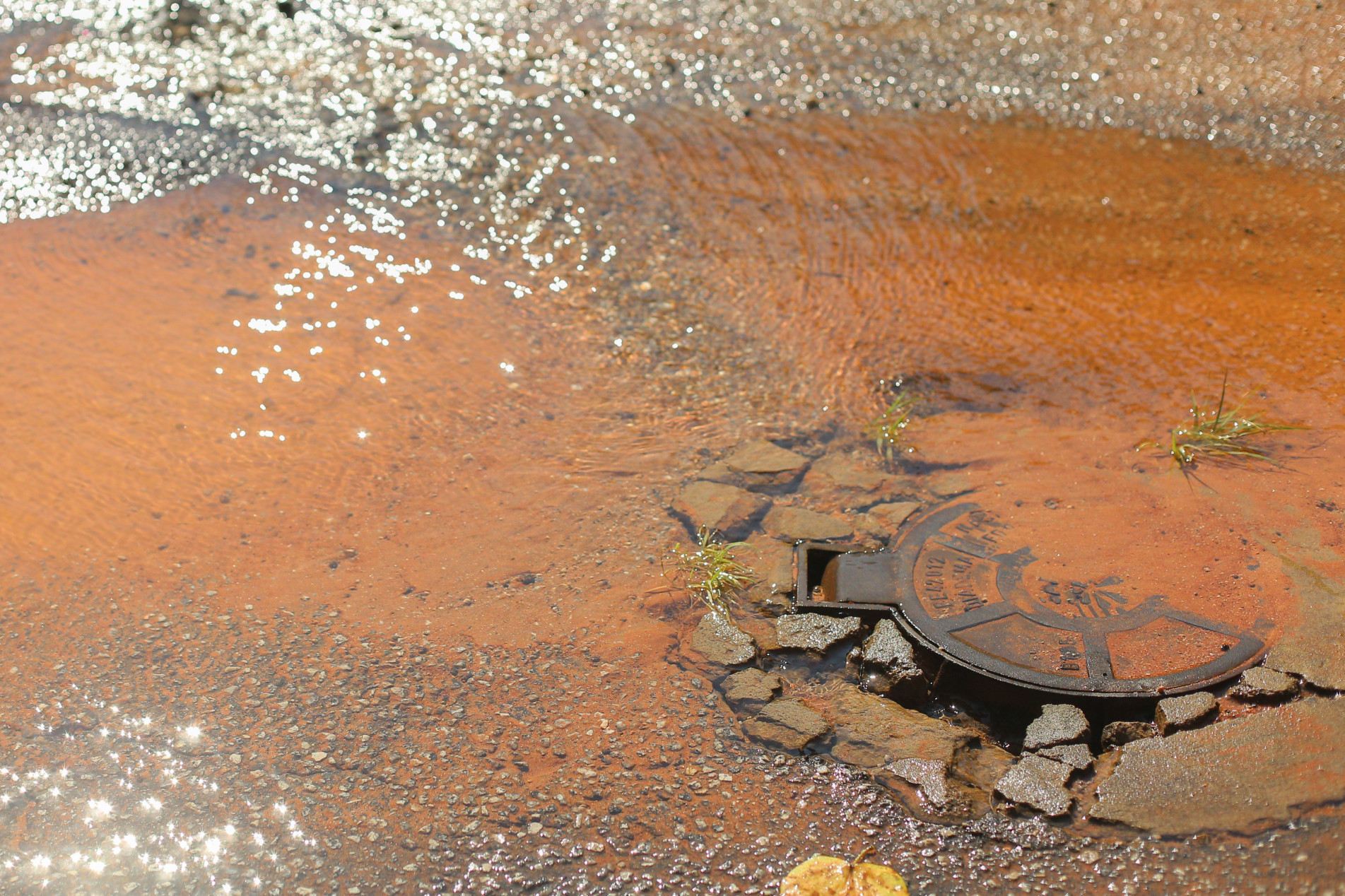 A água limpa escorre constantemente pela rua, formando poças e abrindo um buraco no asfalto



