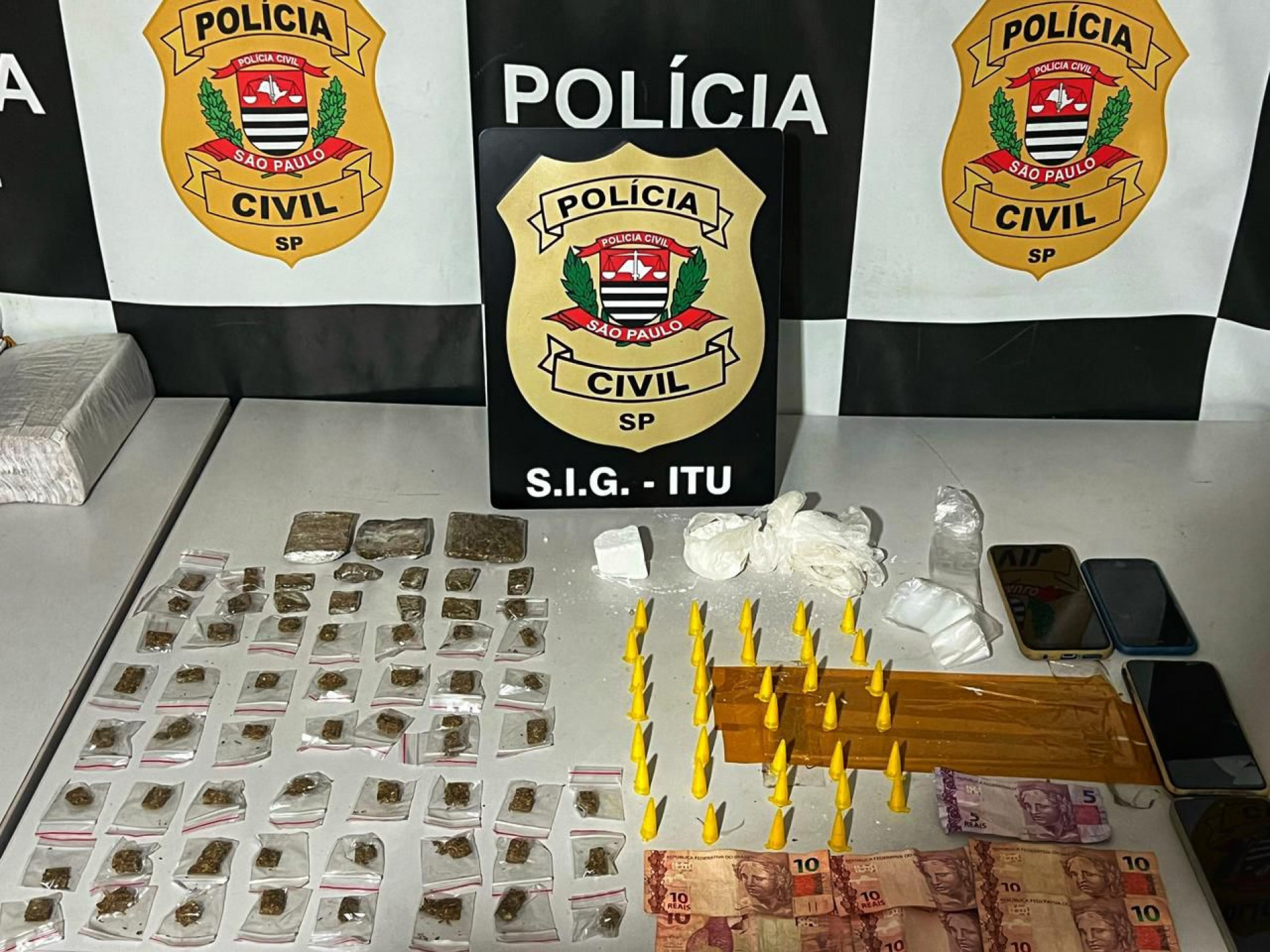 60 porções de maconha prontas para venda, três porções grandes da droga, 34 pinos de cocaína, uma porção a granel, materiais para embalagem e preparo de drogas, além de dinheiro em espécie