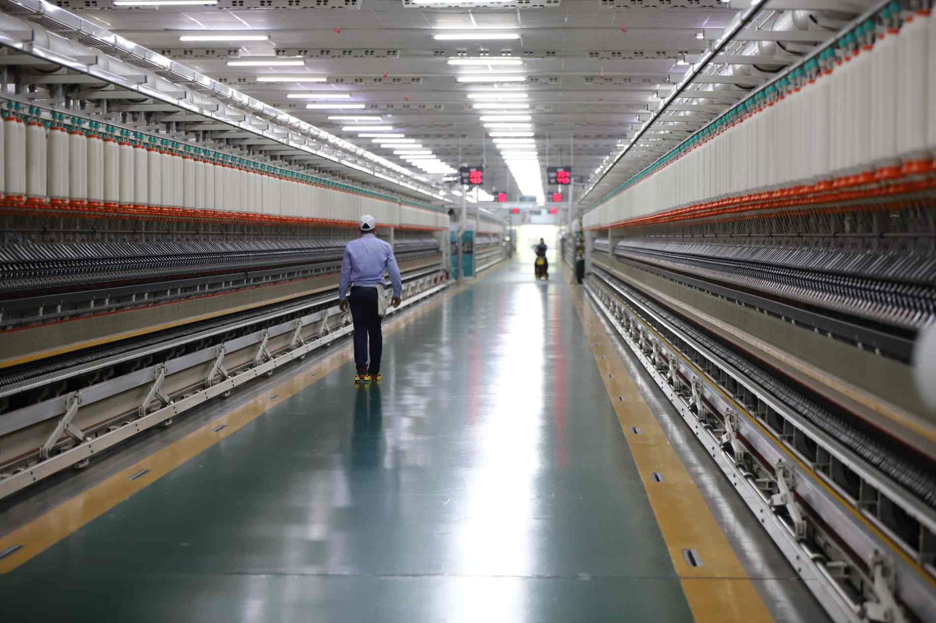 Corredor industrial de uma fábrica moderna, com um funcionário caminhando entre longas fileiras de máquinas automatizadas.