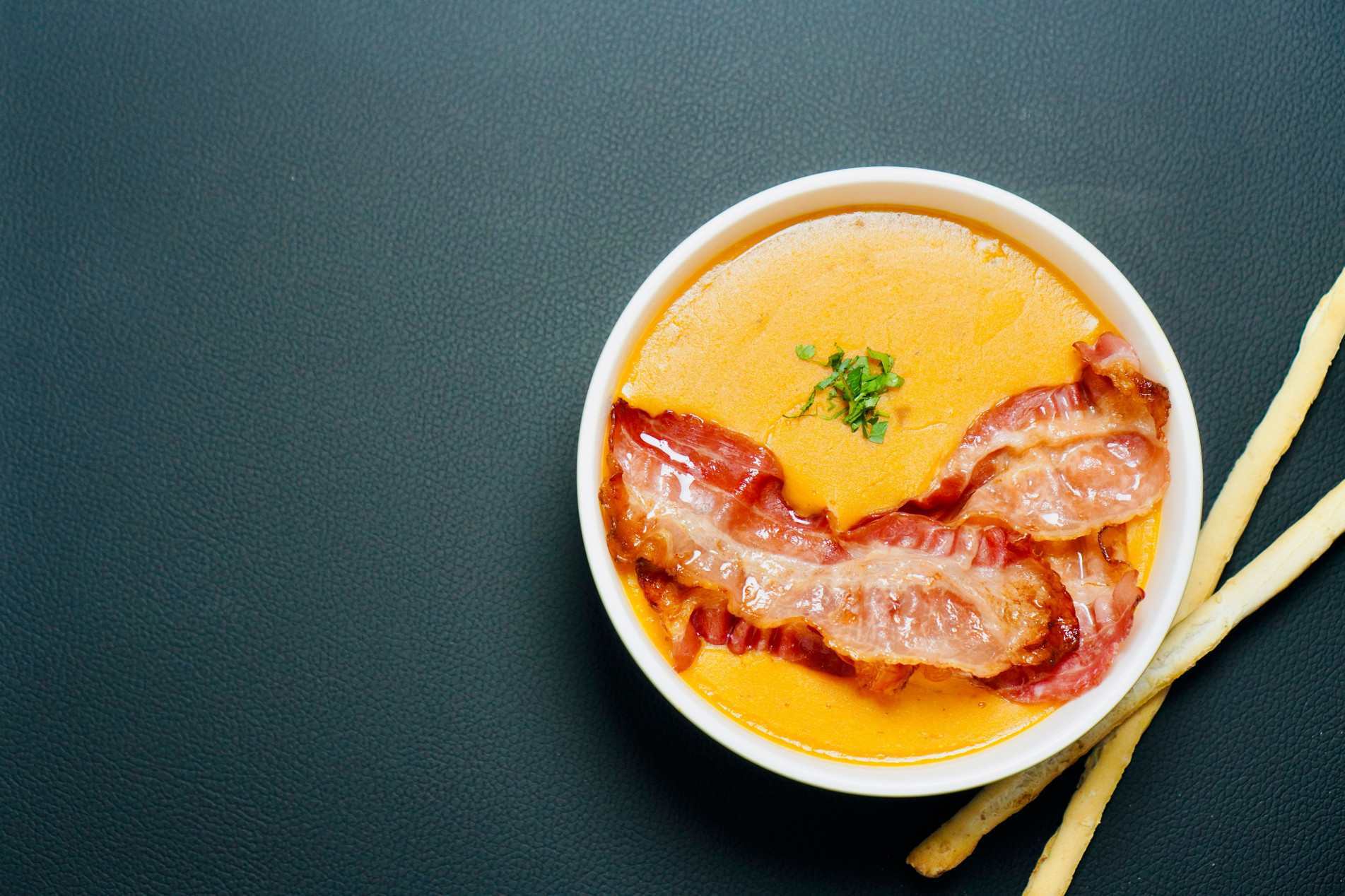 Creme de abóbora low-carb, aveludado, servido com tiras de bacon crocante e finalizado com ervas frescas.