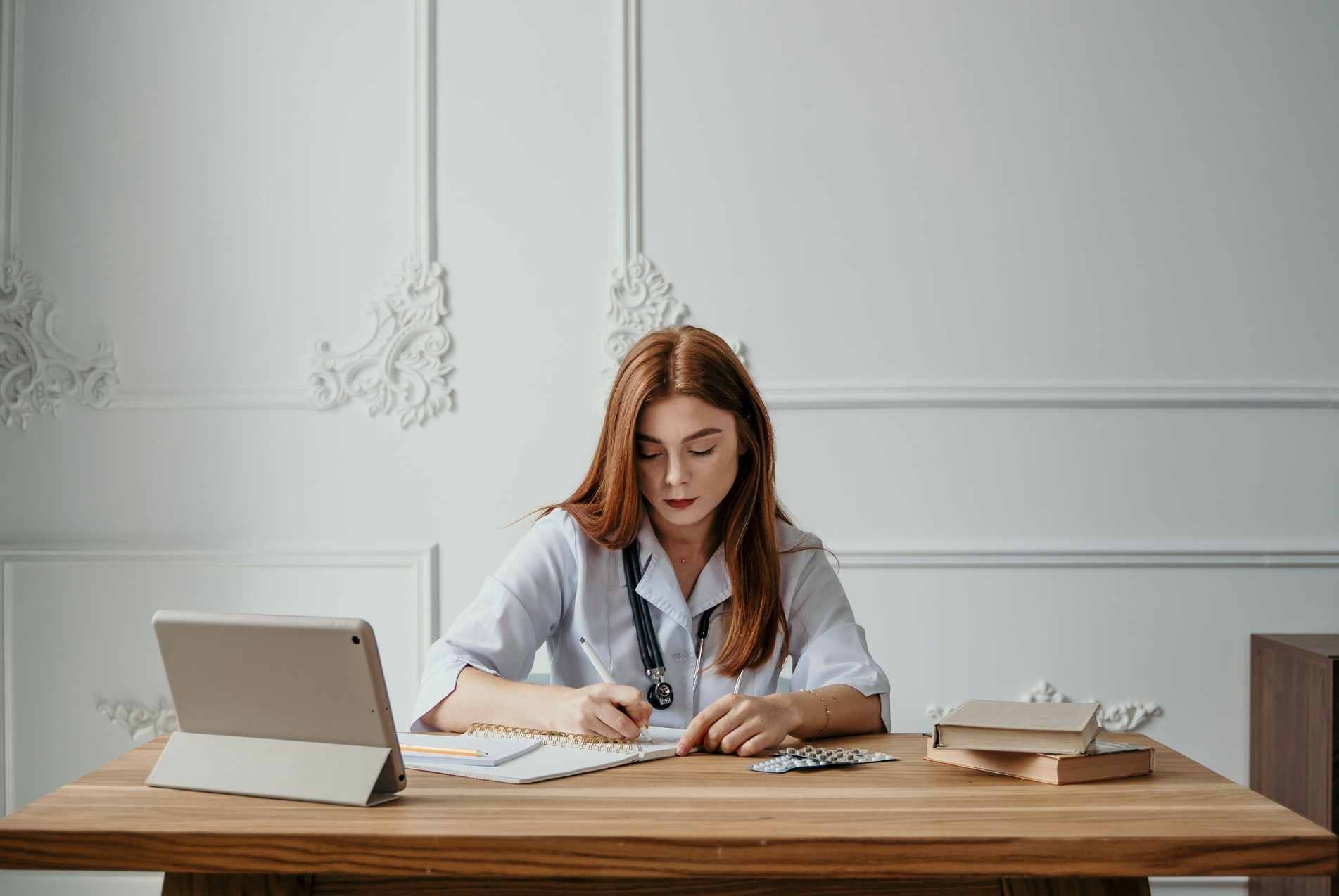 Estudante da área da saúde revisa conteúdos em uma mesa, com tablet, livros e materiais de estudo ao seu redor.