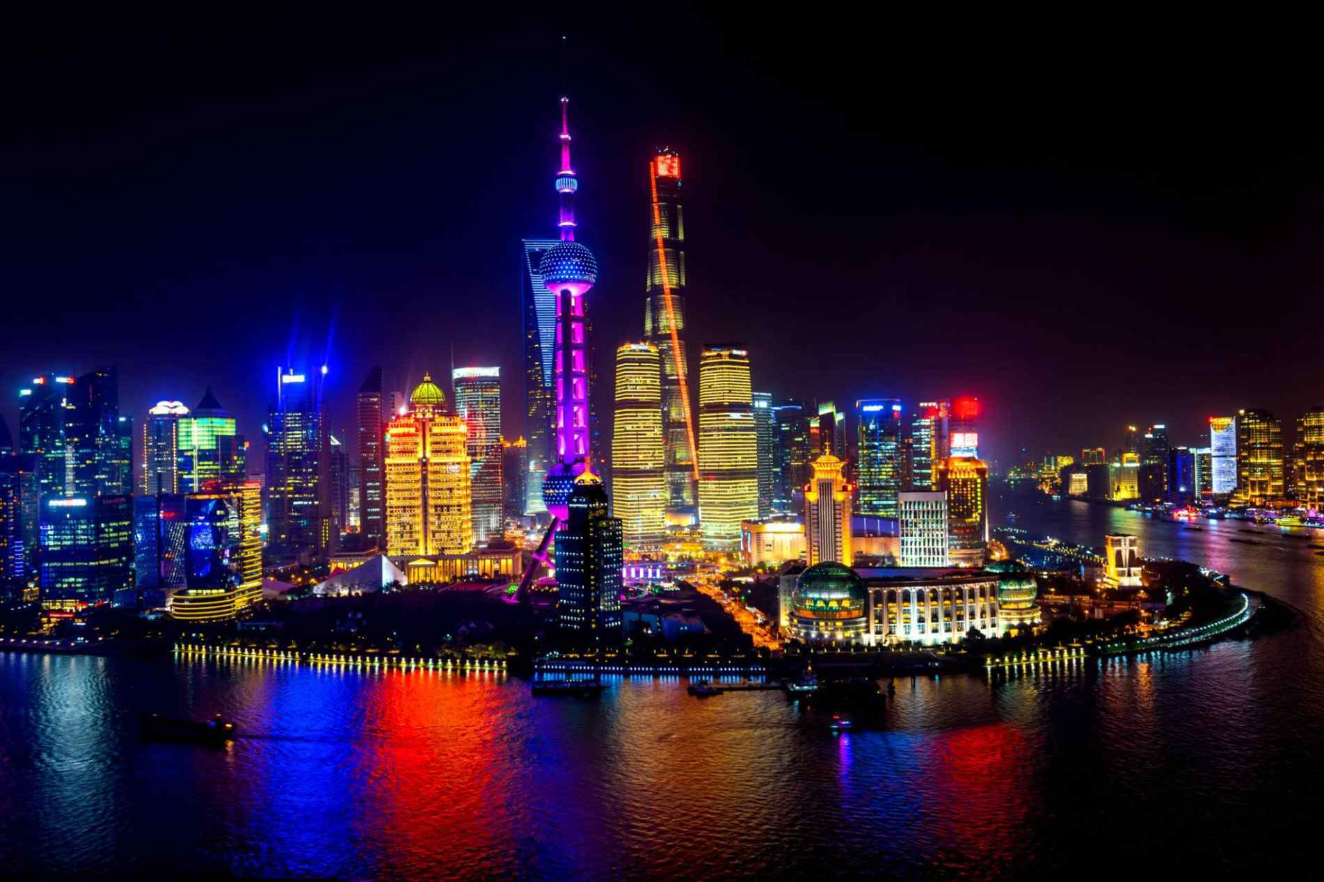 As luzes dos arranha-céus de Xangai refletem no rio Huangpu e mostram o contraste entre a cidade histórica e o futuro da metrópole chinesa