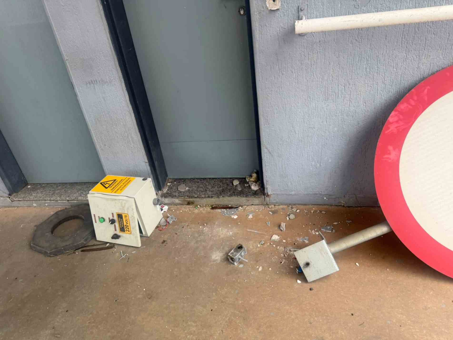Objetos quebrados, como relógio de ponto, placa e partes de pneus, são encontrados na área externa do cômodo